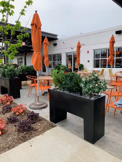 Outdoor patio with black planters, orange chairs, and umbrellas.