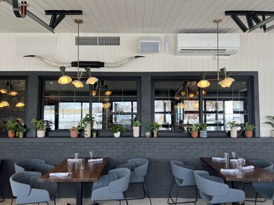 Restaurant interior with grey brick, windowsill plants, longhorn decor, and chandeliers.