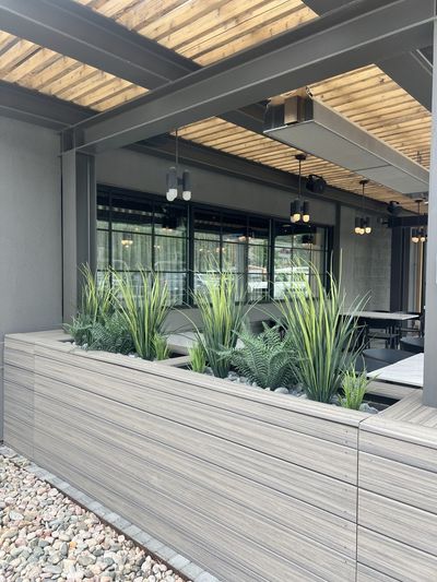 Commercial outdoor patio planter with grasses and ferns beside steel and wood structure.