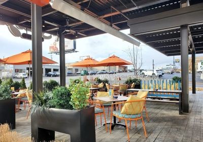 Outdoor dining with large planters and orange umbrellas.