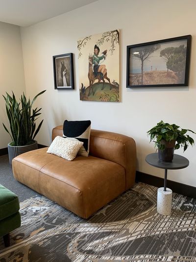 Office lounge with tan leather sofa, snake plant, and gallery wall.