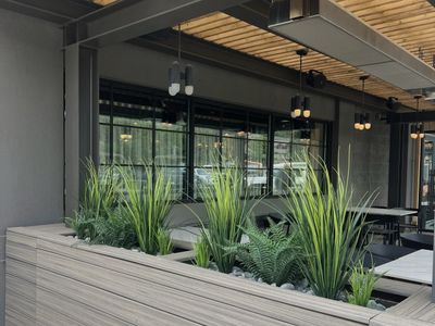 Outdoor patio planter with grasses and ferns under a wood-slat ceiling.